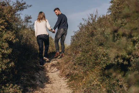 Una pareja camina de la mano por un sendero arenoso rodeado de arbustos verdes en una zona de lodge.