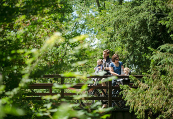 A family enjoys a bike ride through lush greenery at Holiday Park «Kijkduin 9» in the Netherlands.