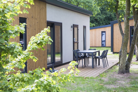 Area esterna del Holiday Park «Kijkduin 1» nei Paesi Bassi con lodge moderni e terrazza con tavolo e sedie.