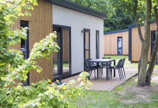 Udendørs område ved Holiday Park «Kijkduin 1» i Holland med moderne træhytter og terrasse med bord og stole.