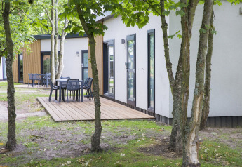 Outdoor terrace with tables and chairs at Holiday Park Kijkduin 1 lodge, surrounded by trees in the Netherlands.