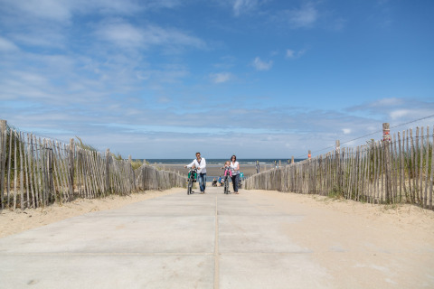 A family walks with bicycles along a sandy path toward the sea at Holiday Park 'Kijkduin 9' in the Netherlands.