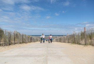 En familie går med deres cykler på en sti til stranden ved Holiday Park 'Kijkduin 9' i Holland.