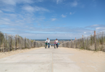 A family walks with bicycles along a sandy path toward the sea at Holiday Park 'Kijkduin 9' in the Netherlands.