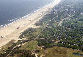 Vista aerea di un lodge sulla spiaggia con bungalow, dune, una strada e l’oceano che si estende lontano.