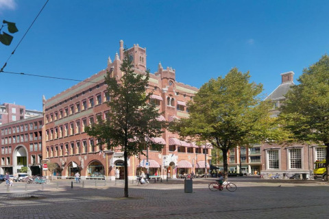 Ein imposantes Hotel in einem historischen Gebäude am Eckplatz mit Bäumen, Fahrrädern und blauem Himmel.