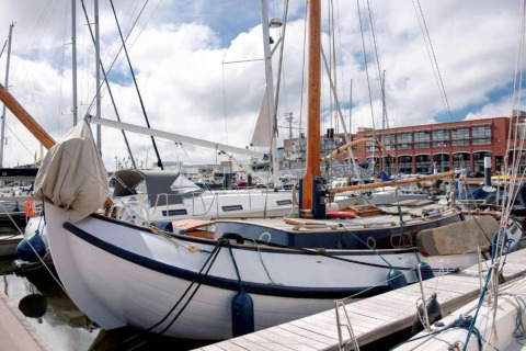 Segelboote vertäut in einem Yachthafen, mit einer roten Backsteinhalle im Hintergrund bei Tageslicht.