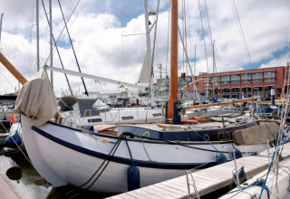 Segelboote vertäut in einem Yachthafen, mit einer roten Backsteinhalle im Hintergrund bei Tageslicht.