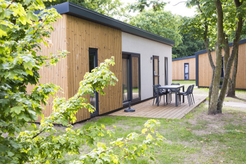 Modern wooden lodge with outdoor patio, table and chairs at Holiday Park 'Kijkduin 1' in the Netherlands.
