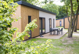 Außenaufnahme einer modernen Holzlodge mit Terrasse und Gartenmöbeln im Holiday Park 'Kijkduin 1', Niederlande.