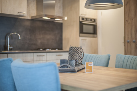 Modern dining area with light blue chairs, wooden table, and kitchen in Holiday Park 'Kijkduin 1', Netherlands.
