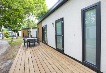 Outdoor deck with dining table at a modern lodge in Holiday Park Kijkduin 1, Netherlands, among trees.