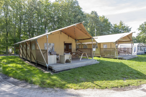Tenda safari presso Holiday Park Klein Vink 21 con veranda in legno, prato verde e alberi circostanti.