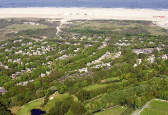 Vista aerea dell'Holiday Park Kijkduin 1 nei Paesi Bassi, con lodge verdi, spiaggia e mare sullo sfondo.