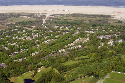 Luftfoto af Holiday Park Kijkduin 1 i Holland, med grønne lodger, strand og hav i baggrunden.