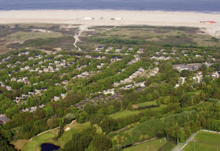 Vista aérea del Holiday Park Kijkduin 1 en los Países Bajos, con lodges verdes, playa y mar al fondo.
