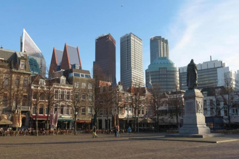 Udsigt over en moderne og klassisk byplads i Nederlandene med skulptur, caféer og høje bygninger.