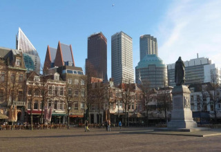 Stadtplatz in den Niederlanden mit Mischung aus moderner Skyline, historischen Gebäuden und Statue.