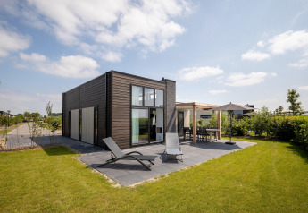 Modern lodge at Holiday Park «Zeedijk 2» in the Netherlands with patio, sun loungers, and a grassy garden.