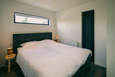 Modern bedroom with a double bed, minimalist decor, and a window at Holiday Park Zeedijk 2 in the Netherlands.