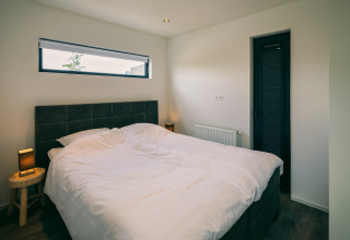 Dormitorio moderno con cama doble, decoración minimalista y ventana en Holiday Park Zeedijk 2, Países Bajos.