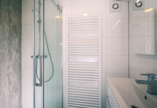 Modernes Badezimmer in einer Lodge mit Duschkabine, Waschbecken, Handtuchheizkörper und weißen Fliesen.