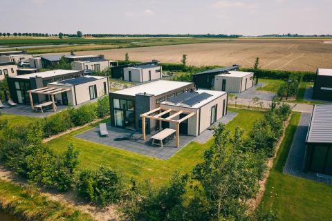 Vista aerea di lodge moderni con pannelli solari, giardini privati e campi sullo sfondo.