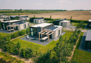 Luftfoto af moderne lodgehytter med solpaneler, grønne haver og landbrugsmarker i baggrunden.