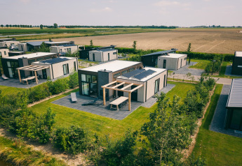 Aerial view of modern lodge cabins with solar panels, private gardens, and fields in the background.
