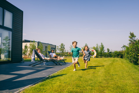 Due bambini corrono sull’erba presso un lodge, mentre due adulti si rilassano sulle sdraio sul patio.