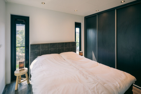 Modern bedroom at Holiday Park Zeedijk 2 in the Netherlands with a double bed and large black closets.