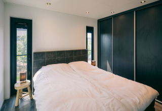 Dormitorio moderno en Holiday Park Zeedijk 2, Países Bajos, con cama doble y armarios negros grandes.