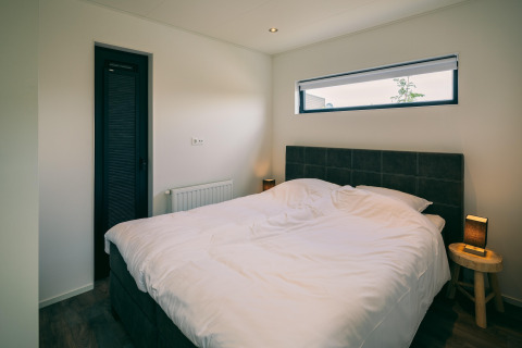 Chambre avec lit double, draps blancs, tables de chevet et fenêtre au Holiday Park Zeedijk 2, Pays-Bas.