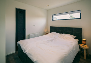 Camera da letto con letto matrimoniale, biancheria bianca, tavolini e finestra al Holiday Park Zeedijk 2, Paesi Bassi.