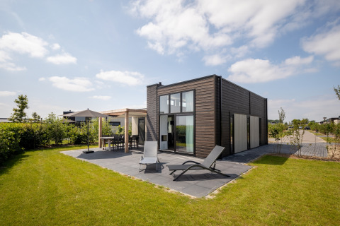 Lodge moderne au Holiday Park Zeedijk 2, Pays-Bas, avec pelouse, chaises longues et terrasse extérieure.