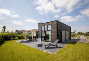 Modern lodge at Holiday Park Zeedijk 2 in the Netherlands, featuring lawn, patio chairs, and umbrellas.