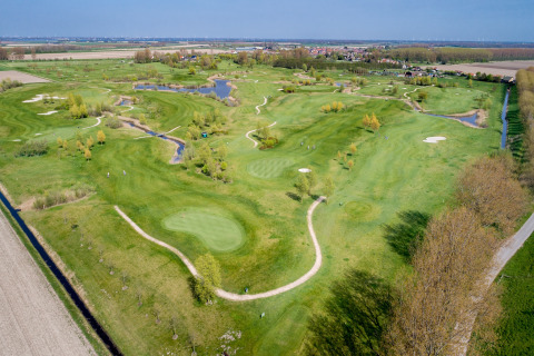 Vista aerea di un campo da golf verde con sentieri, laghetti e alberi vicino a un lodge e a un paese.