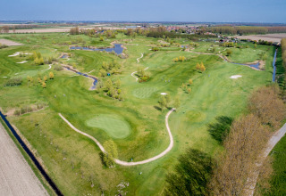 Vista aerea di un campo da golf verde con sentieri, laghetti e alberi vicino a un lodge e a un paese.