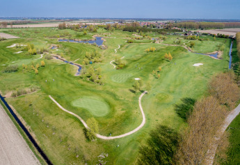 Aerial view of a lush golf course with winding paths, ponds, and trees near a lodge and village.