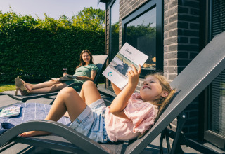 Una bambina e una donna si rilassano su sdraio, leggono libri e si godono il sole davanti a un lodge.