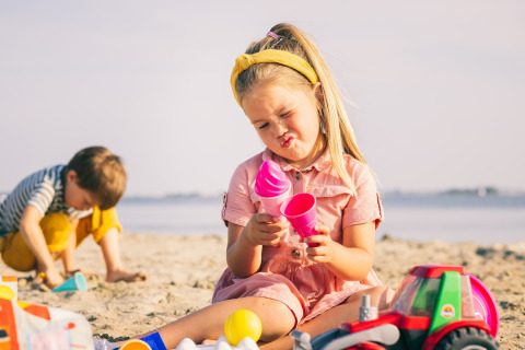 Deux enfants jouent avec des jouets dans le sable à la plage. La fille fait une grimace amusante, le garçon creuse.