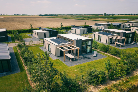 Vue aérienne du Holiday Park Zeedijk 2 aux Pays-Bas avec chalets modernes, pelouses et champs agricoles.