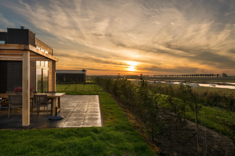 Sunset at Holiday Park Zeedijk 2 lodge in the Netherlands, featuring a terrace, green lawn, and river view.