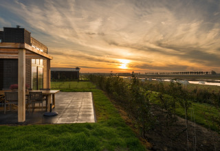 Atardecer en la cabaña Holiday Park Zeedijk 2 en Países Bajos, con terraza, césped y río al fondo.