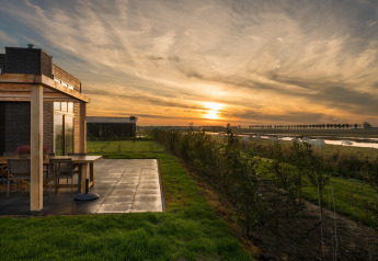 Sunset at Holiday Park Zeedijk 2 lodge in the Netherlands, featuring a terrace, green lawn, and river view.