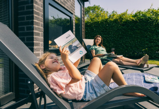 Mor og datter slapper af på liggestole udenfor en lodge i Holiday Park Zeedijk 2, Holland, nyder solskin og bøger.
