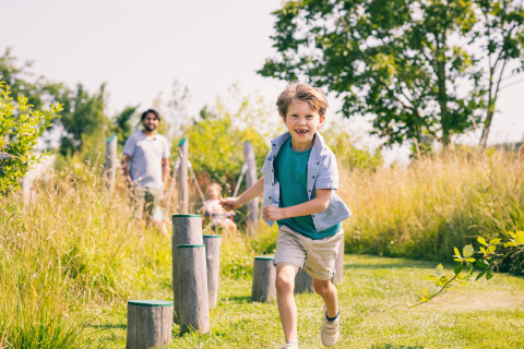 Niño sonriente corriendo al aire libre en Holiday Park Zeedijk 2 en los Países Bajos, adultos detrás observando.