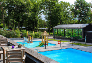 Zona glamping all’aperto con piscine, area giochi per bambini e alberi verdi in una giornata di sole.