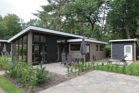 Moderne lodge ved Holiday Park De Rimboe & De Woeste Hoogte 25 med terrasse, havemøbler og grønt område.