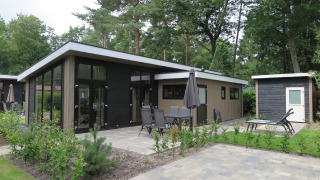 Moderne lodge ved Holiday Park De Rimboe & De Woeste Hoogte 25 med terrasse, havemøbler og grønt område.
